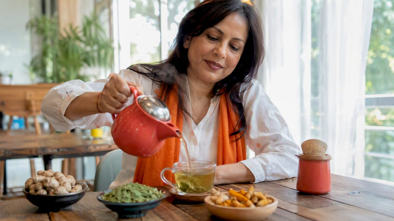 Woman brewing anti-inflammatory turmeric-ginger tea at kitchen table