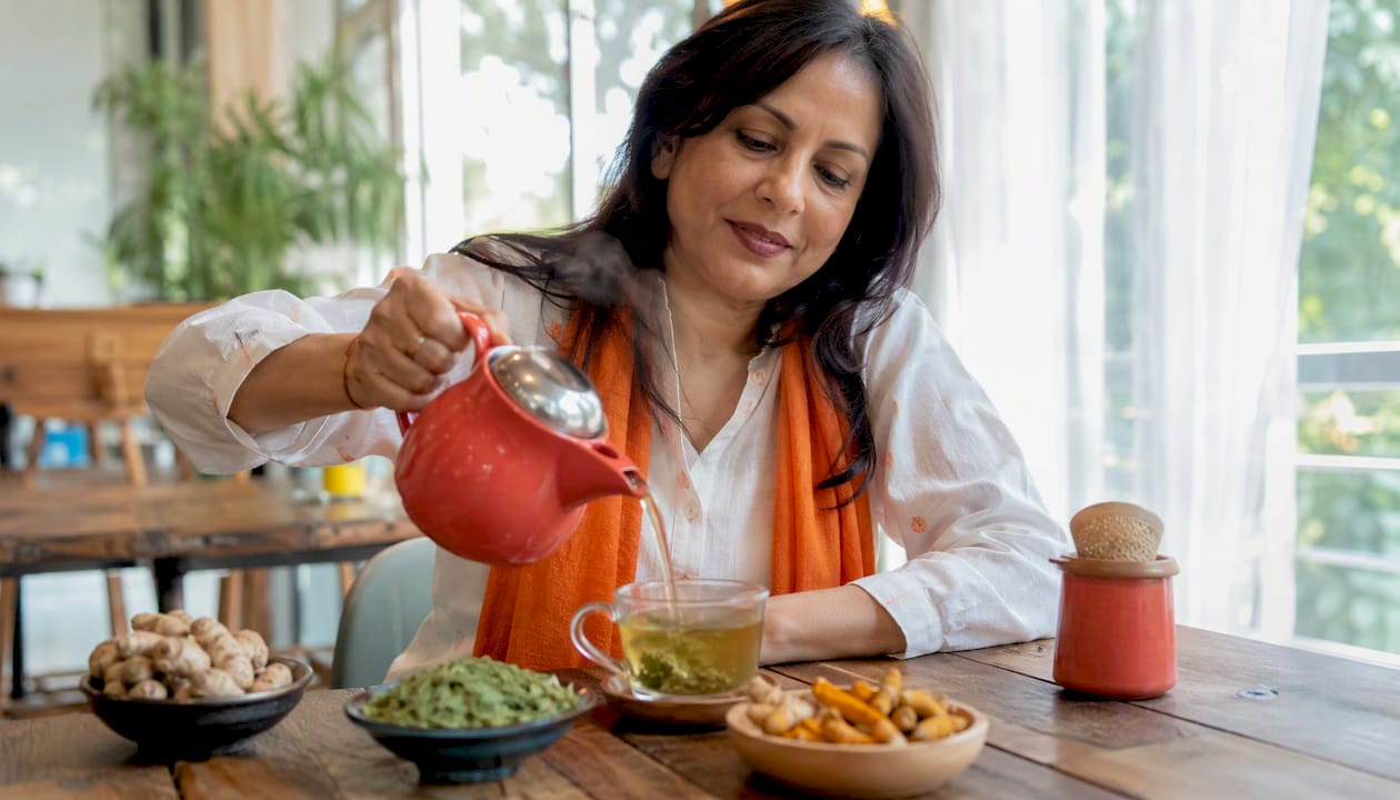 Woman brewing anti-inflammatory turmeric-ginger tea at kitchen table