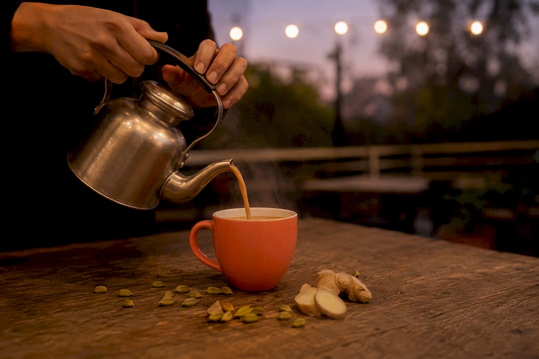 Hand pouring steaming chai with spices