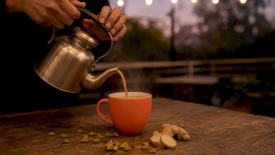 Hand pouring steaming chai with spices